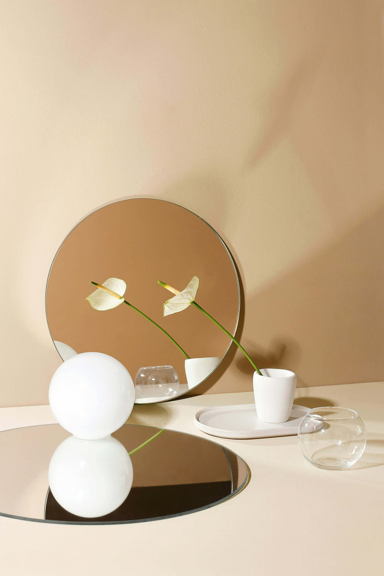 Modern vase and sleek glass decor on reflective surface with elegant mirror backdrop in contemporary home setting.