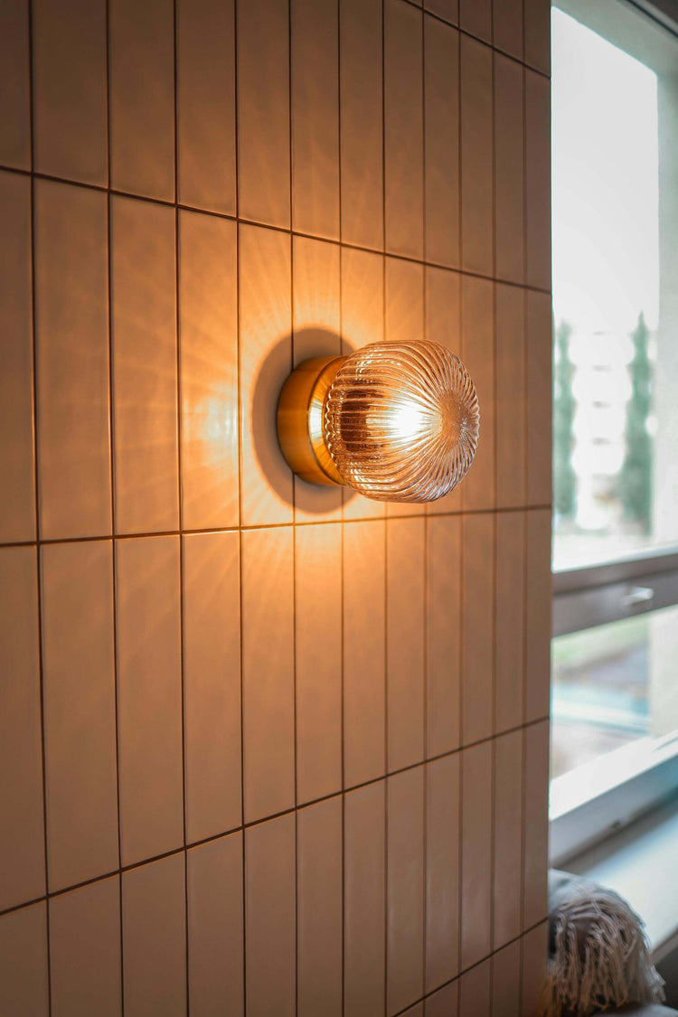 Elegant wall-mounted luminaire illuminating a tiled wall with warm light in a modern interior setting.