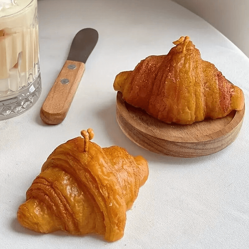 Bougie parfumée en forme de croissant sur table, accompagnée d'un couteau et d'une boisson, idéale pour une décoration élégante.