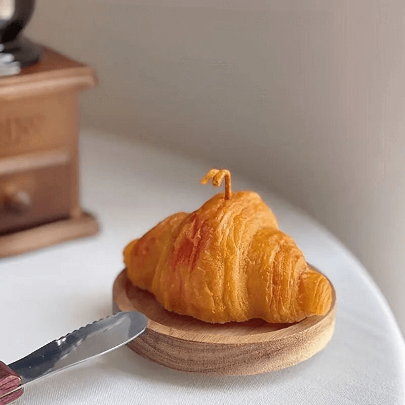 Bougie parfumée en forme de croissant sur une table avec un couteau et une boîte en bois en arrière-plan