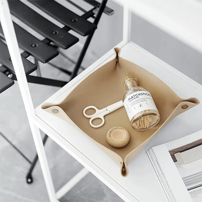 Elegant brown leather catchall tray on white shelf with small items like scissors, vial, and wooden accessory, perfect for home organization.