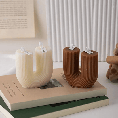 Deux bougies aromatiques en forme de U, une blanche et une marron, reposant sur des livres pour une décoration intérieure scandinave élégante.