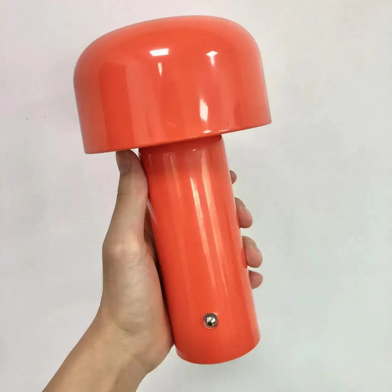 Main holding LED mini champignon table lamp in vibrant orange color.