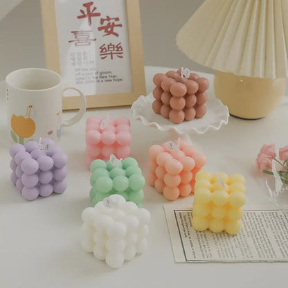 Collection of colorful handmade Rubik's cube-shaped soy wax candles on a table.