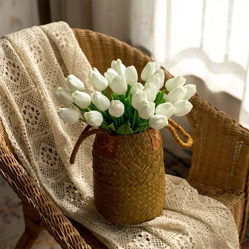 Magnifique bouquet de tulipes en soie blanches dans un vase en osier, posé sur une chaise en rotin décorée d'une couverture en dentelle.