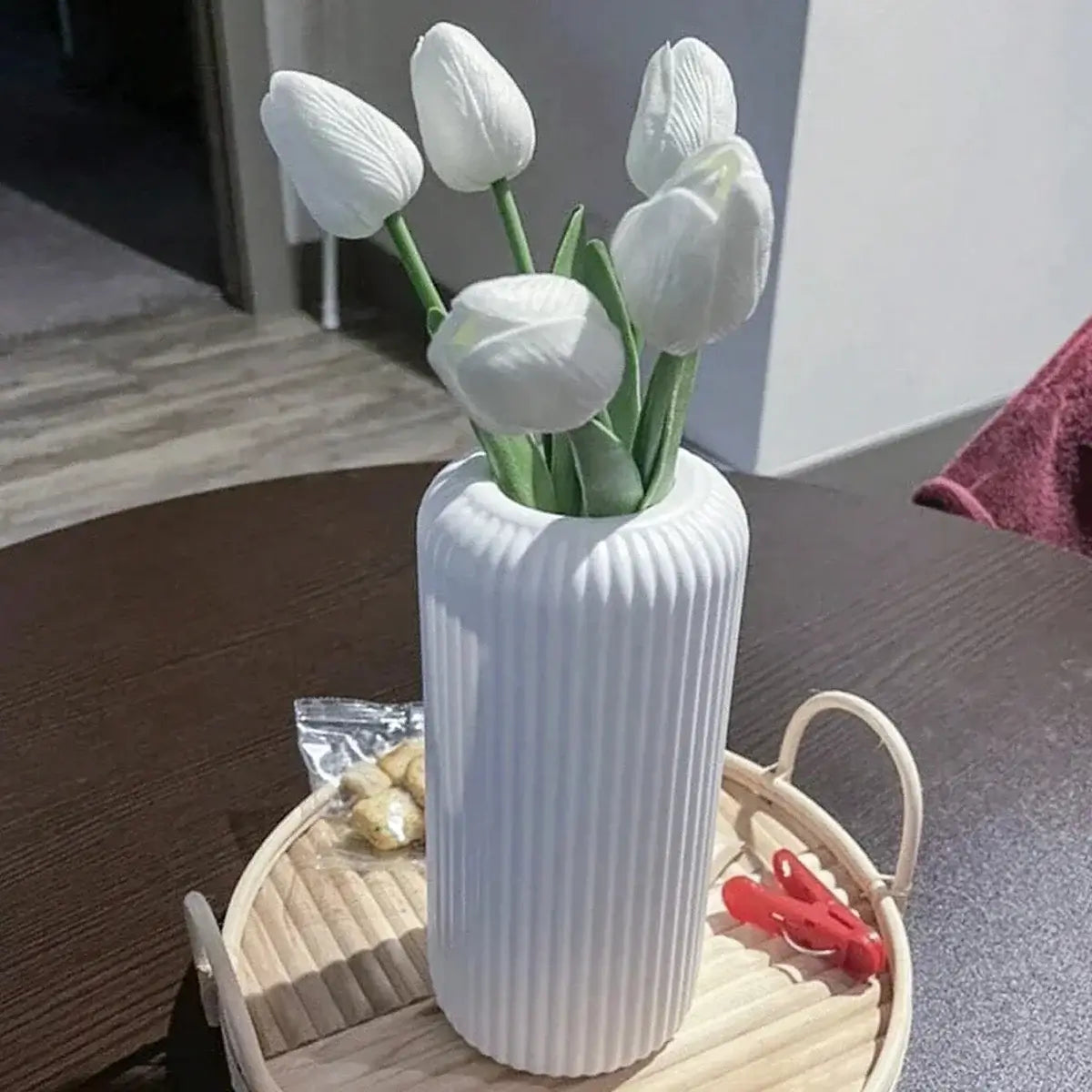 Vase en plastique rayé effet céramique avec fleurs blanches, sur une table en bois, ajoutant une touche d'élégance à la décoration intérieure.