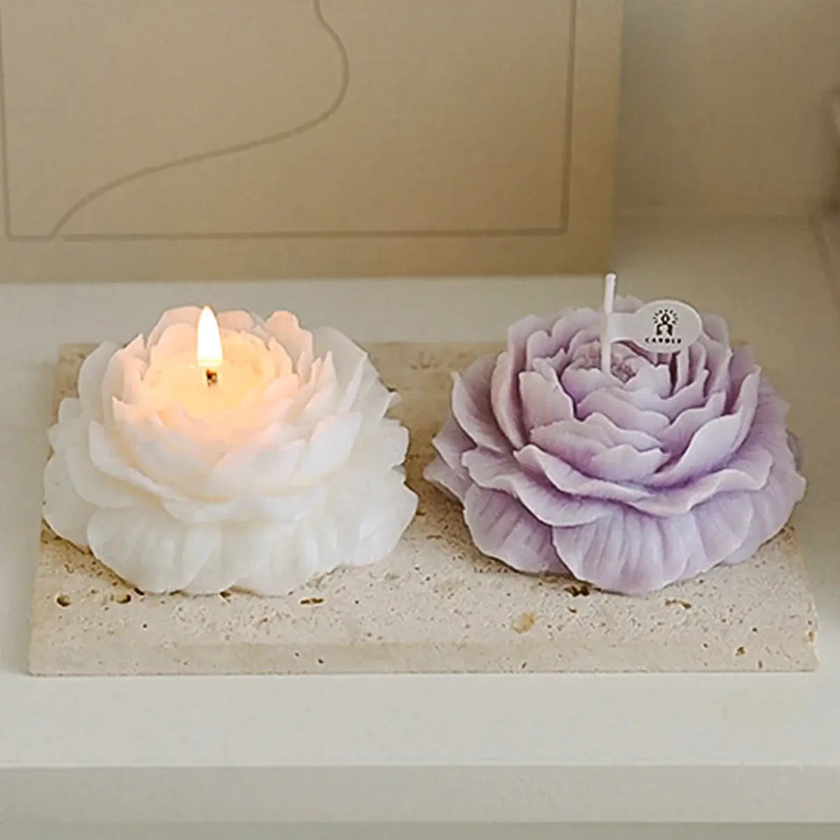 Aromatherapy rose-shaped candles, one lit white and one purple, on a stone tray for a romantic and relaxing ambiance.