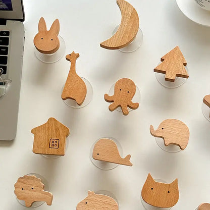 Decorative wooden animal hooks and shapes including a giraffe, elephant, whale, cat, and more, arranged on a table near a laptop.