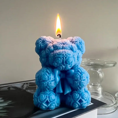 Bougie en forme d'ours en peluche, bleue, faite de roses en cire, allumée et posée sur une surface élégante.