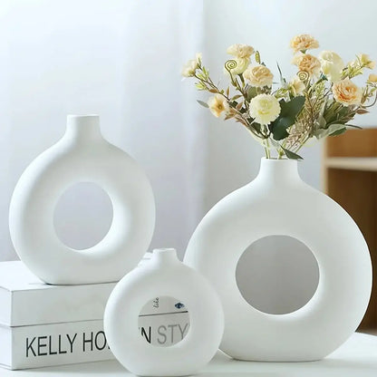 Trois vases en céramique blanche en forme de donut, contenant des fleurs séchées, parfaits pour une décoration intérieure minimaliste et moderne.