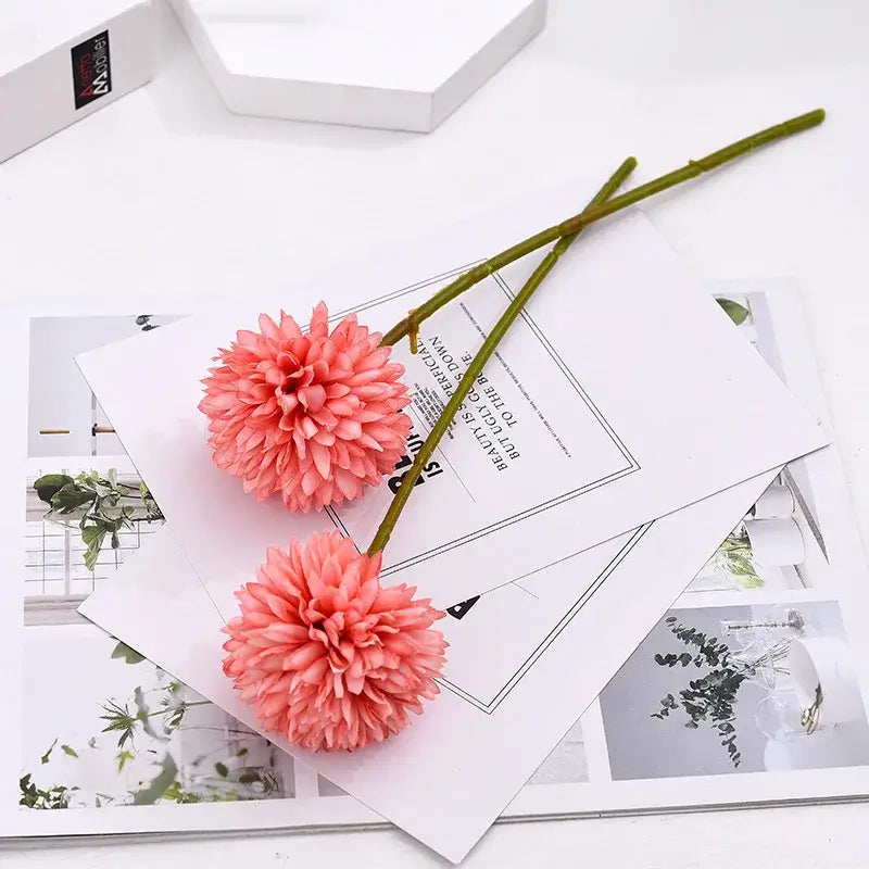 Two pink silk chrysanthemum stems placed on decorative papers, adding an elegant touch to the setting.