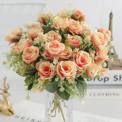 Bouquet de roses en soie rose-orange avec de la verdure dans un vase en verre, idéal pour la décoration intérieure et les mariages.