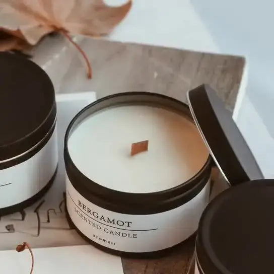 Bergamot scented candle in a black matte jar with a wooden wick, placed on a rustic background with fall leaf decor.