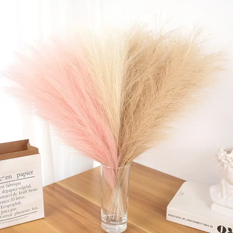 Bouquet de tiges de pampas multicolores dans un vase en verre sur une table en bois – décoration élégante et naturelle pour événements ou intérieur.