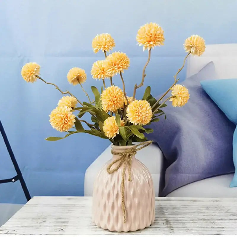 Bouquet de fleurs artificielles pissenlit dans un vase texturé sur une table en bois blanc, décor idéal pour mariage et maison.