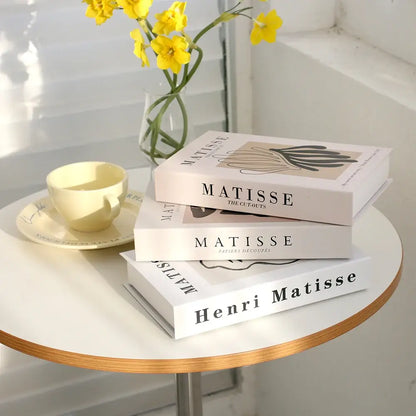 Faux livres de décoration art moderne empilés sur une table avec tasse et fleurs jaunes