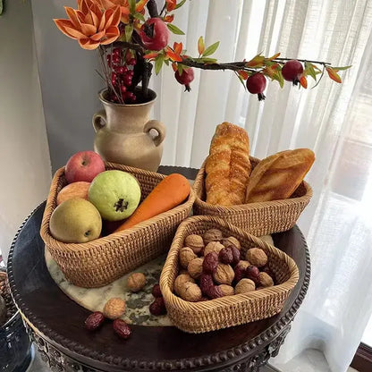 Panier de rangement en osier tressé avec fruits, noix et pain sur une table en bois, décoré avec un vase de fleurs.