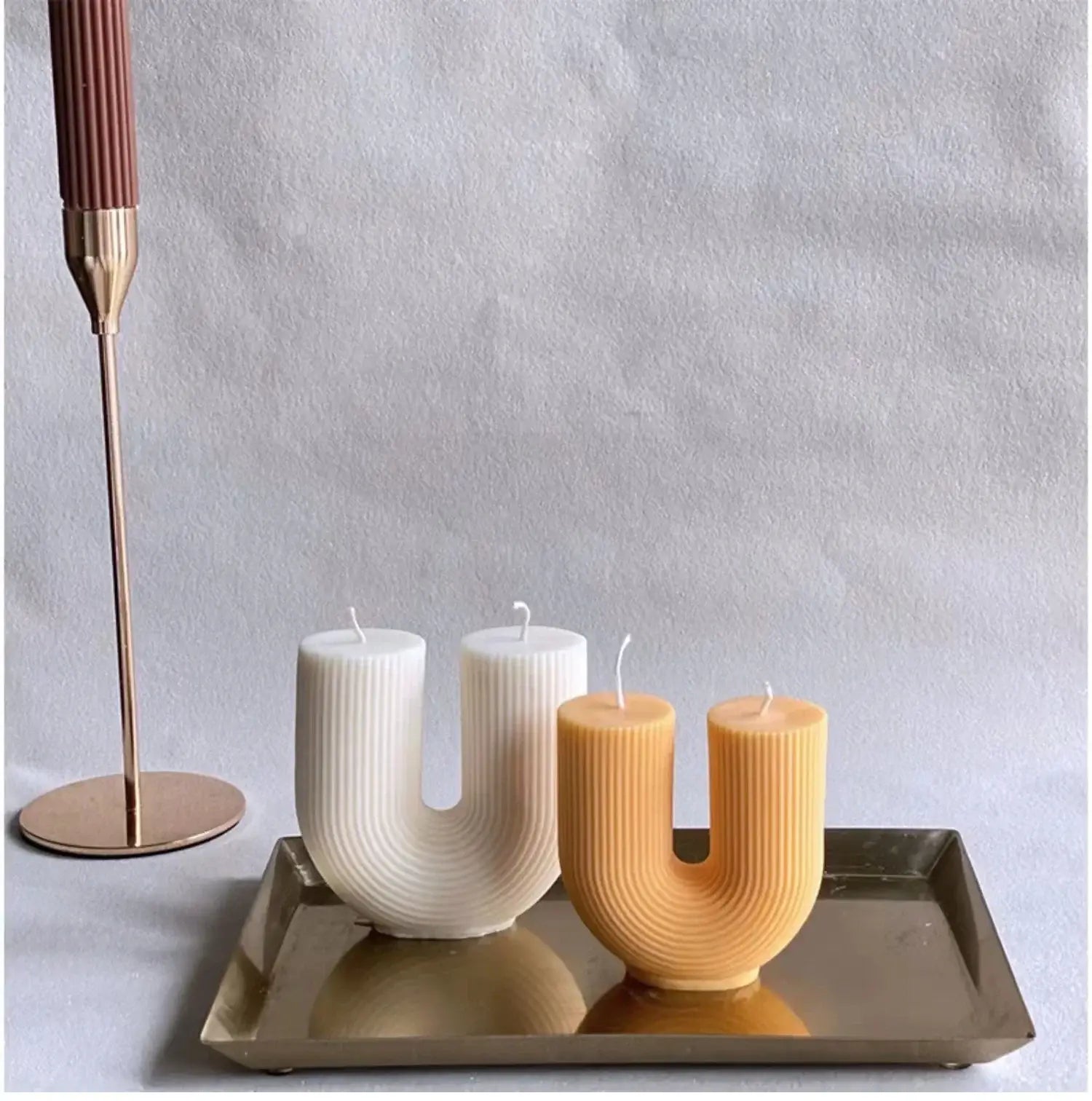 Handmade U-shaped soy wax candles with modern design in white and yellow, displayed on a metallic tray next to a chic candle holder.