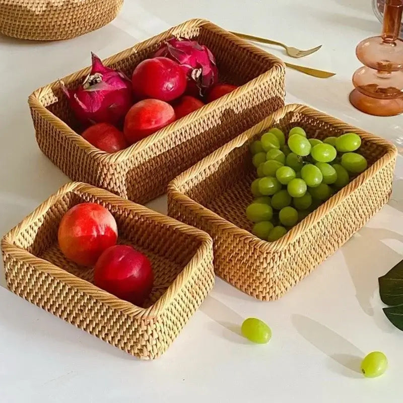 Trois paniers de rangement en osier tressé contenant des fruits colorés sur une table blanche.