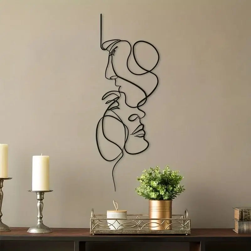 Métal décoration murale avec deux visages, design moderne minimaliste pour intérieur élégant, fixé sur un mur beige près de bougies et plante.