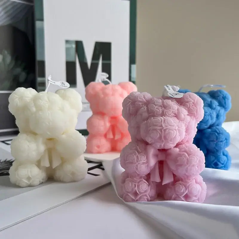 Teddy bear-shaped scented candles made from rose designs in white, pink, and blue colors displayed on a table.