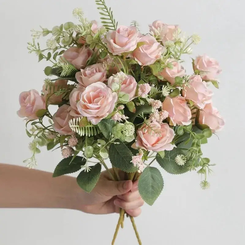 Bouquet de roses artificielles en soie, de couleur rose pâle, tenu dans la main, idéal pour mariages et décoration intérieure.