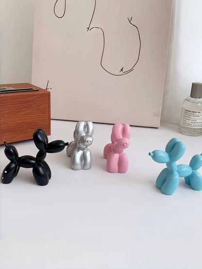 Quatre statuettes de chien en ballon en résine de différentes couleurs sur une table, parfaites pour une décoration intérieure ludique.