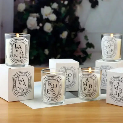 Display of elegantly packaged aromatic candles labeled Lavande, Rose, and Ambre, set on a wooden surface with a floral backdrop.