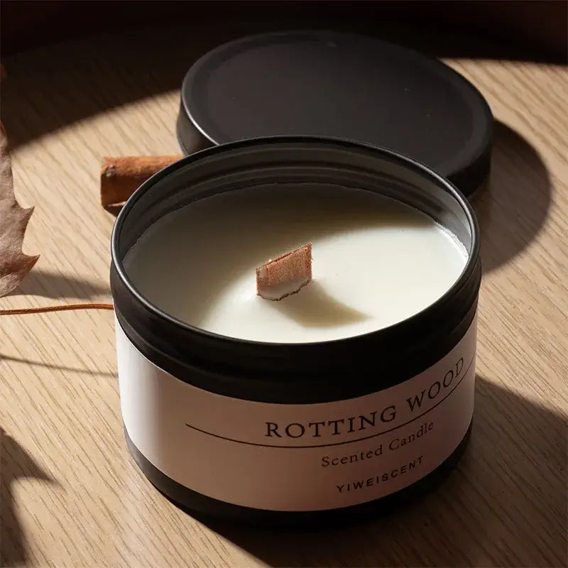 Bougie parfumée en pot noir mat avec mèche en bois et étiquette "Rotting Wood" sur une table en bois.