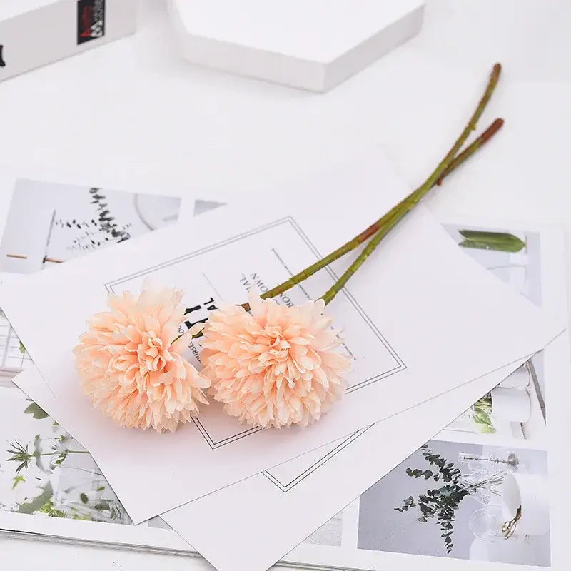 Two delicate pink chrysanthemum silk flowers on a white surface, perfect for home decoration and special occasions.