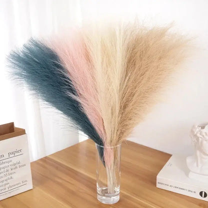 Bouquet de tiges de pampas multicolores dans un vase en verre sur une table en bois, décoration élégante pour événements et intérieur.