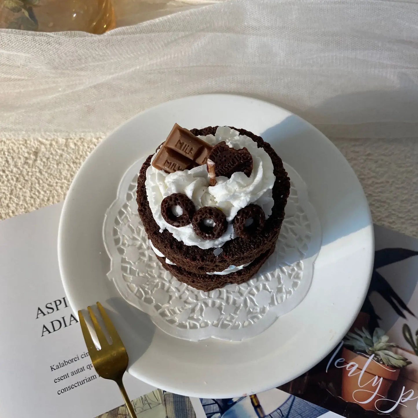 Bougie parfumée gâteau sur assiette blanche avec décorations en chocolat et chantilly, parfait pour un intérieur gourmand et chaleureux