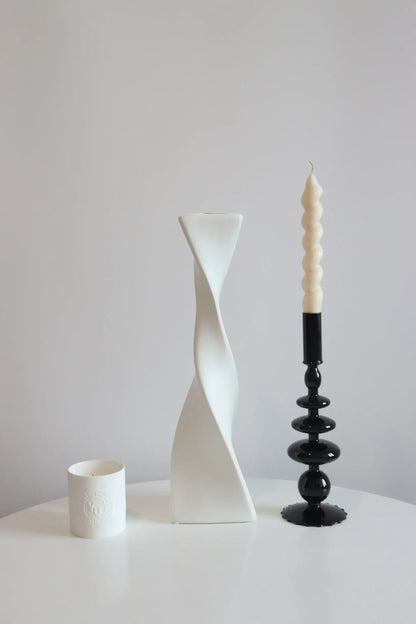 Bougie d'aromathérapie en cire d'abeille bâton spirale sur un support noir moderne à côté de vases décoratifs minimalistes.