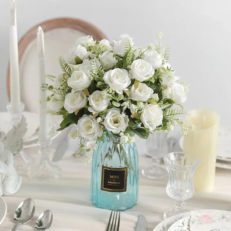 Bouquet de roses artificielles en soie blanche dans un vase bleu sur une table décorée pour un événement.