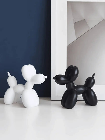 Deux statues en résine de chiens ballons blanc et noir posées sur une table devant un cadre, décoration ludique et originale pour intérieur.