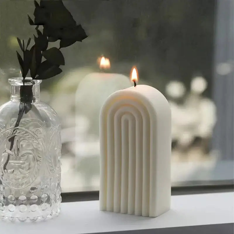 Bougie d'aromathérapie en cire de soja au design sculptural allumée, posée à côté d'un vase en verre sur un rebord de fenêtre.