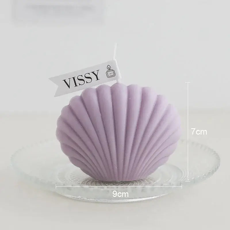 Bougie parfumée en forme de coquillage violette en cire de soja sur un plat en verre, mesurant 9 cm de large et 7 cm de haut