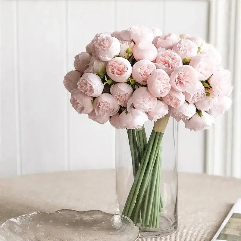 Bouquet de pivoines en soie rose réalistes avec 27 têtes de roses dans un vase en verre, ajoutant une touche d'élégance à la décoration intérieure.