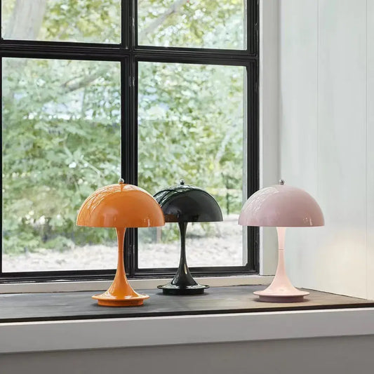 Lampe de table moderne en aluminium dans des couleurs orange, noir et rose sur le rebord d'une fenêtre, apportant une touche d'élégance minimaliste.