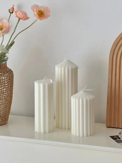 Bougies géométriques parfumées blanches avec design cylindrique sur une table, à côté de fleurs et décoration intérieure.