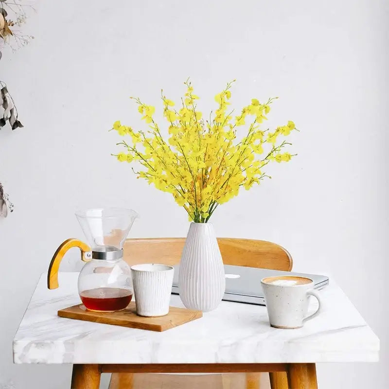 Elegant yellow orchid bouquet in white vase on marble table with coffee and laptop