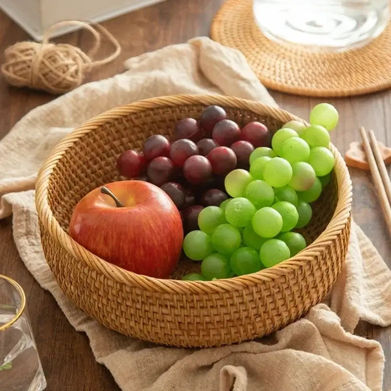 Woven wicker basket with red apple and green and purple grapes on a wooden table.