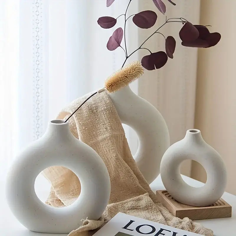 Elegant white ceramic donut vases beautifully arranged with dried flowers on a table, showcasing minimalist design and modern home decor.