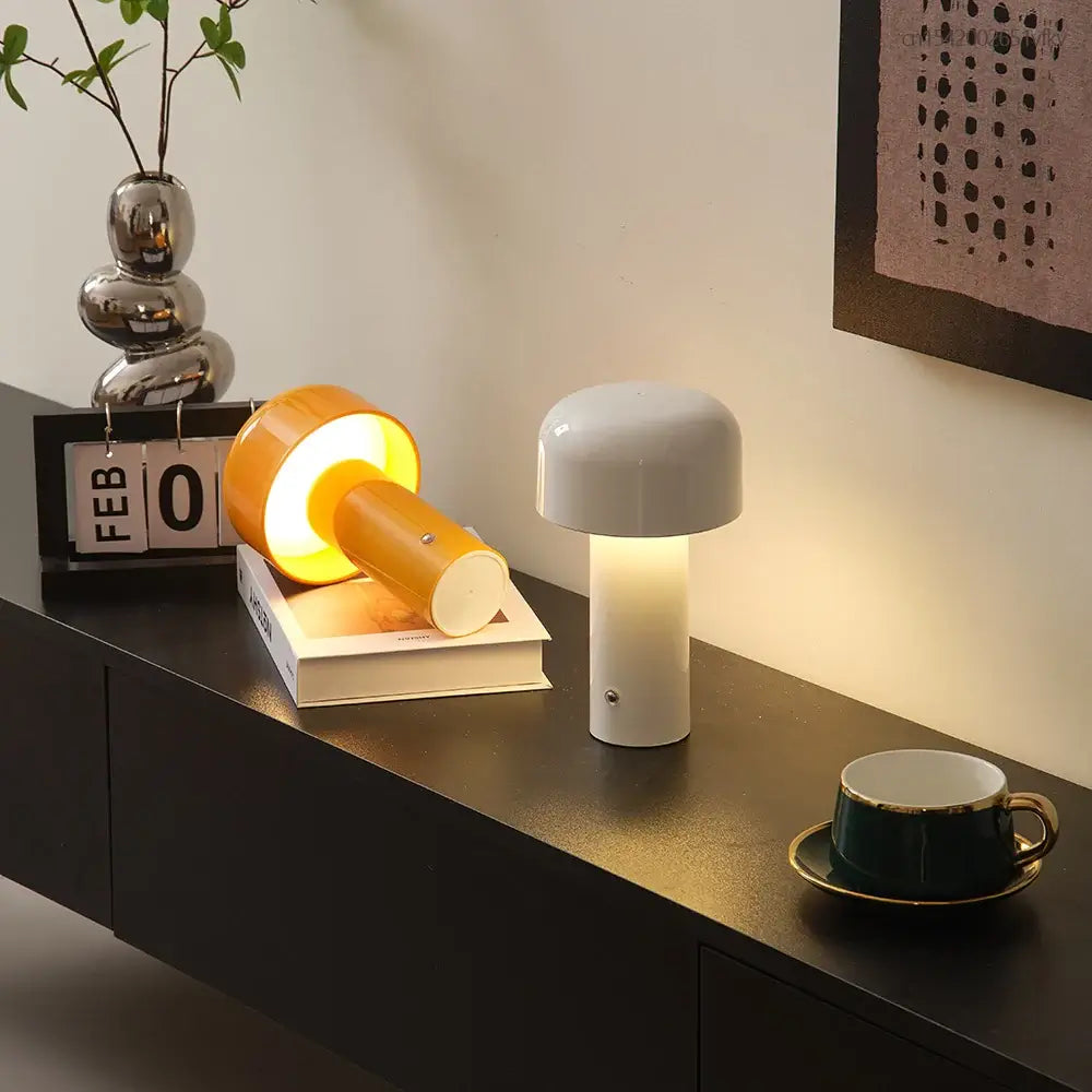 Lampe de table LED mini champignon allumée et éteinte sur une étagère noire, avec une tasse à café et des objets décoratifs adjacents.